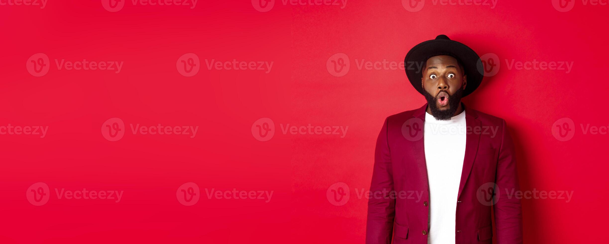 Fashion and party concept. Impressed Black man in classy outfit staring with complete disbelief at camera, gasping and looking surprised, standing over red background photo