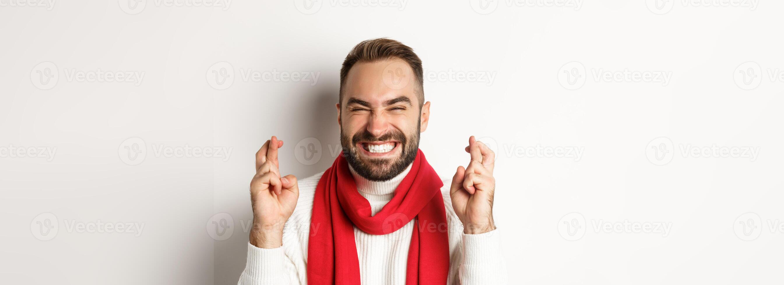 Christmas holidays. Happy attractive man making wish on winter holidays, cross fingers for good luck, standing over white background photo