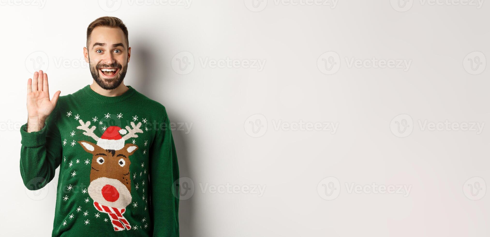 New Year, holidays and celebration. Friendly young man waving hand and greeting people at Christmas party, saying hello, standing over white background photo