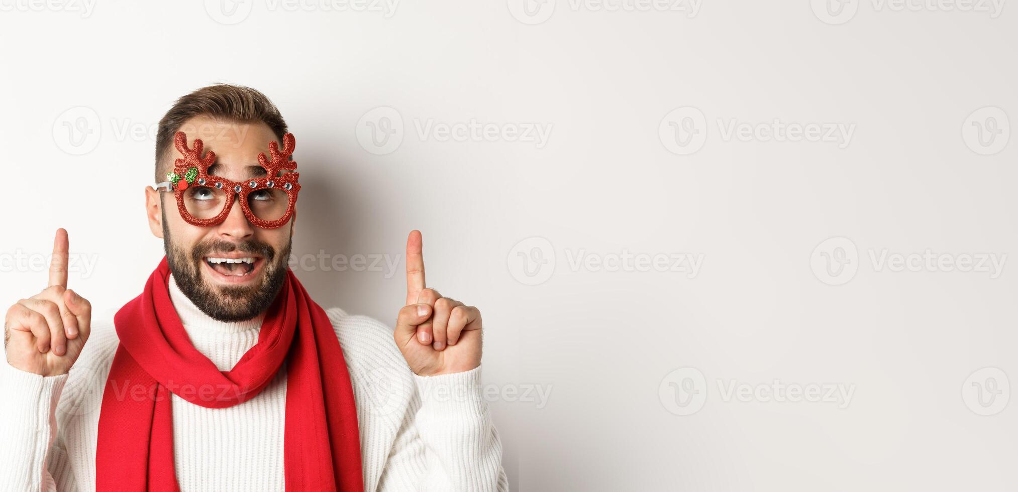Christmas, New Year and celebration concept. Close-up of excited bearded guy in party glasses, pointing and looking up at store promo, white background photo