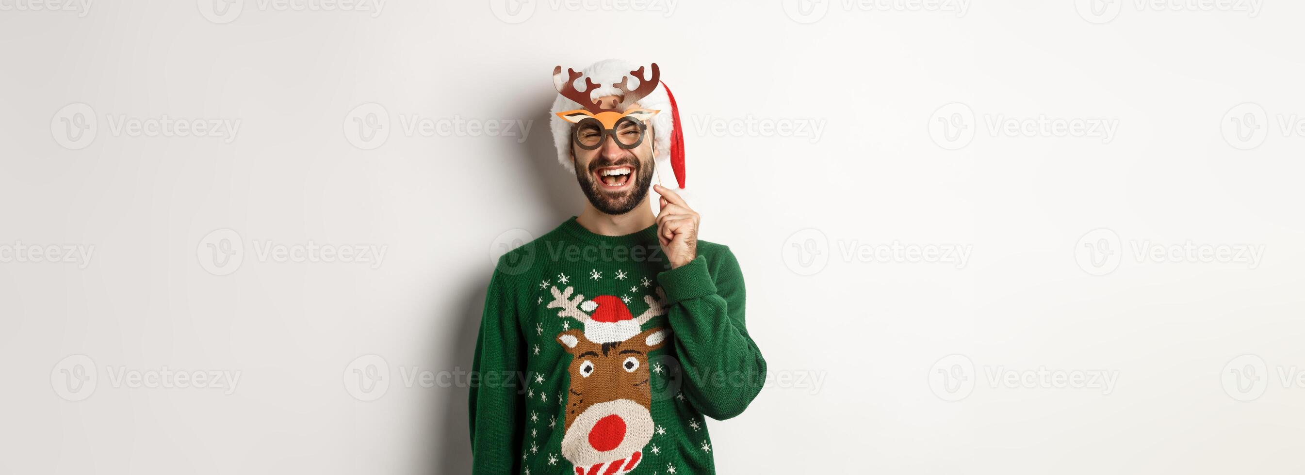 Christmas and holidays concept. Smiling beared man in Santa hat looking happy, holding party mask for New Year, celebrating xmas, standing over white background photo