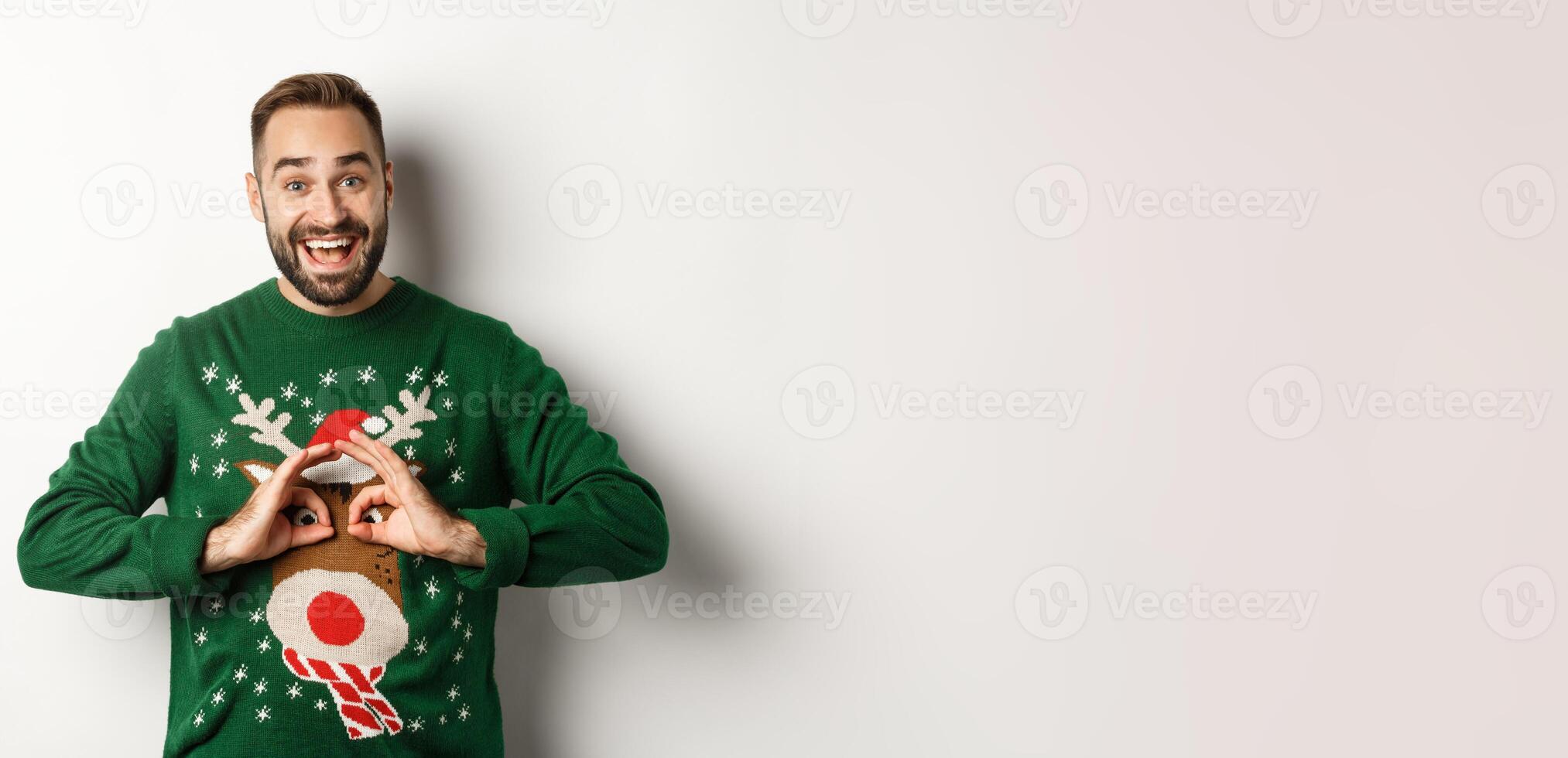 New Year, holidays and celebration. Happy young man making fun of his sweater and smiling, fool around on Christmas party, standing over white background photo