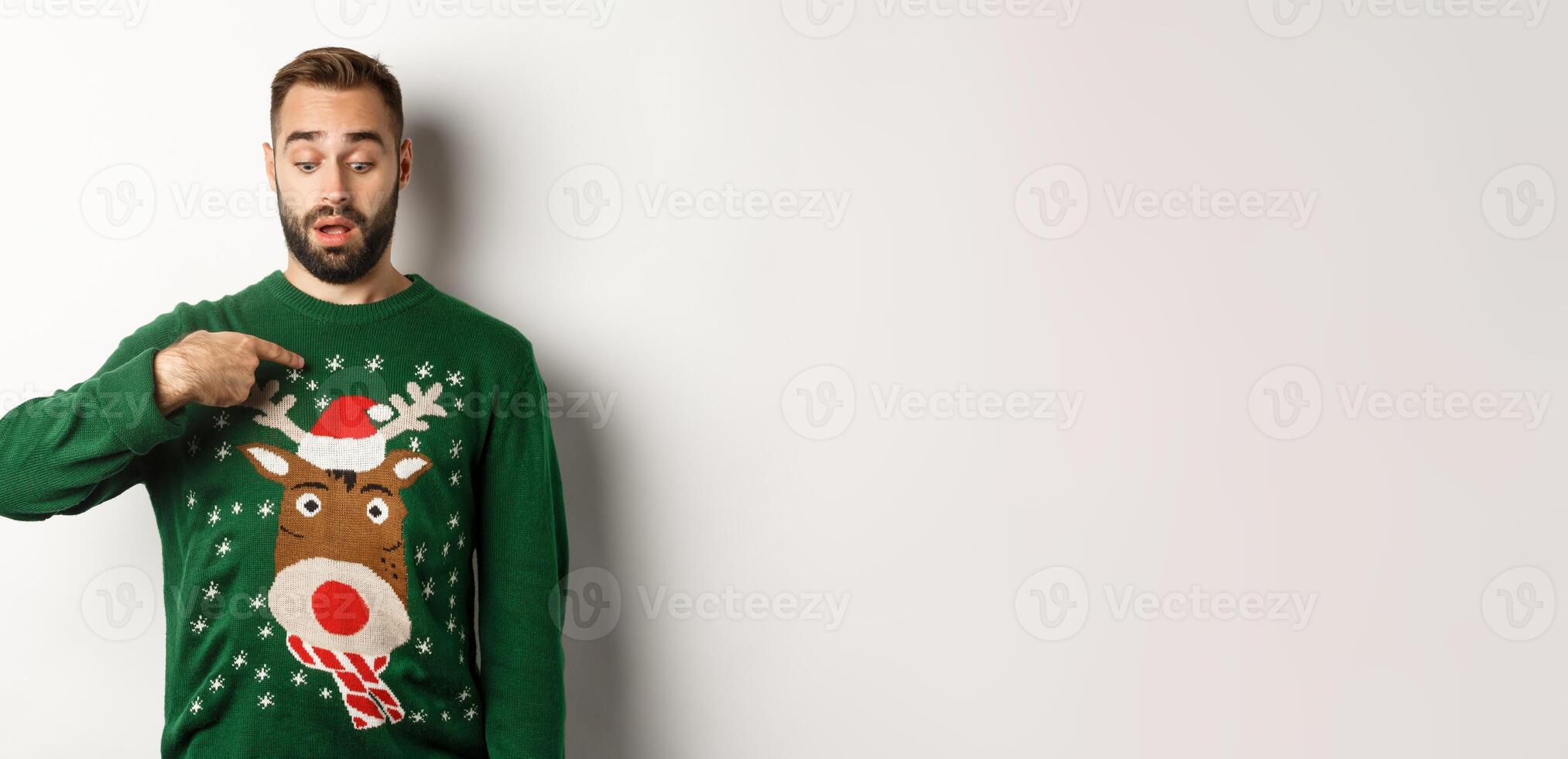 Winter holidays and christmas. Confused guy in sweater pointing at himself, standing puzzled over white background photo