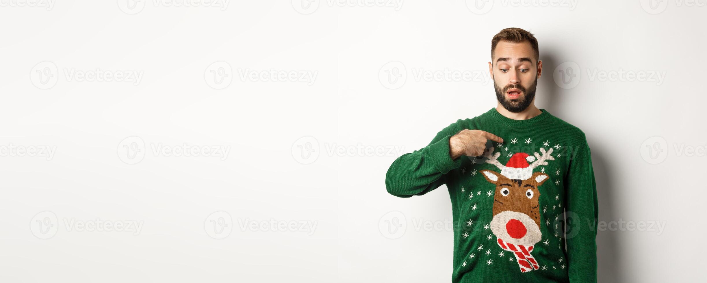 Winter holidays and christmas. Confused guy in sweater pointing at himself, standing puzzled over white background photo