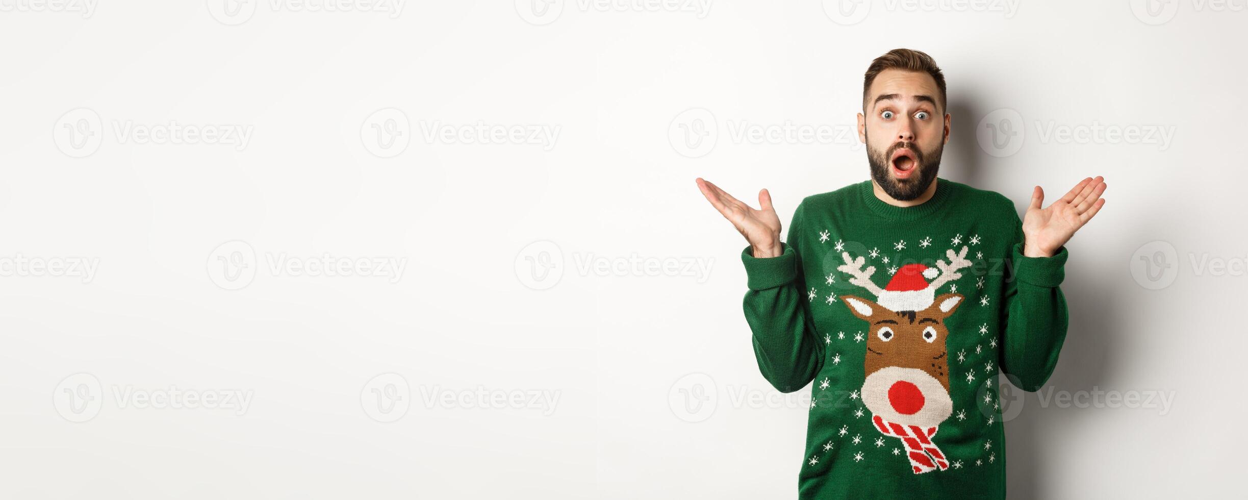 New Year party and winter holidays concept. Surprised bearded guy gasping amazed, standing in Christmas sweater, white background photo