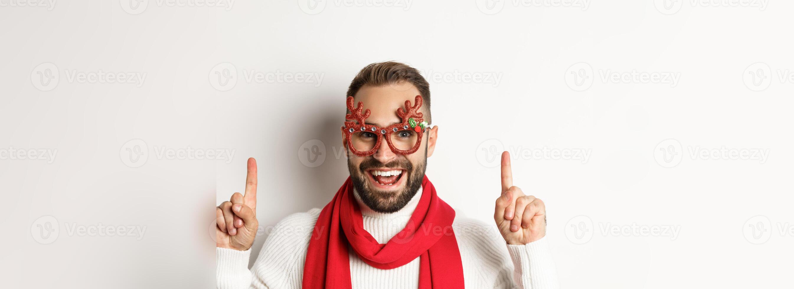 Christmas, New Year and celebration concept. Close-up of handsome bearded man in party glasses and red scarf, celebrate winter holidays and pointing fingers up at copy space photo