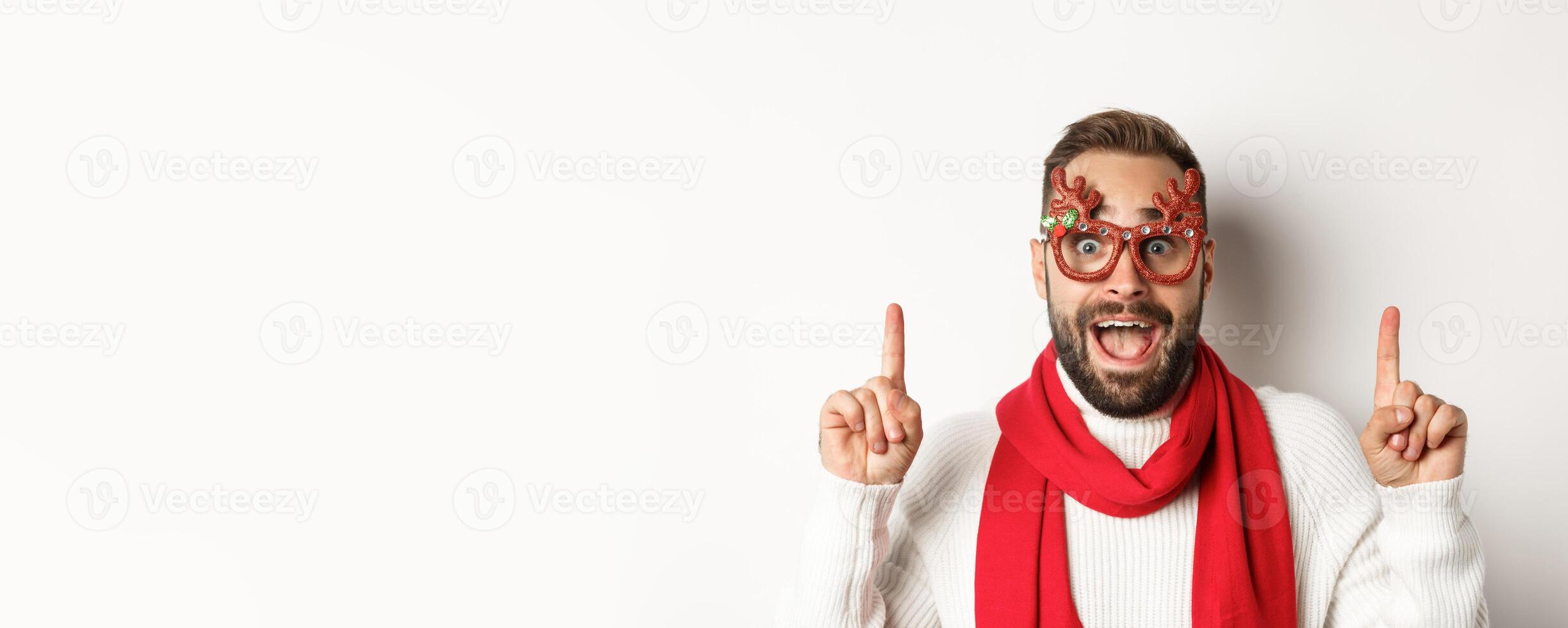 Christmas, New Year and celebration concept. Close-up of handsome bearded man in party glasses and red scarf, celebrate winter holidays and pointing fingers up at copy space photo