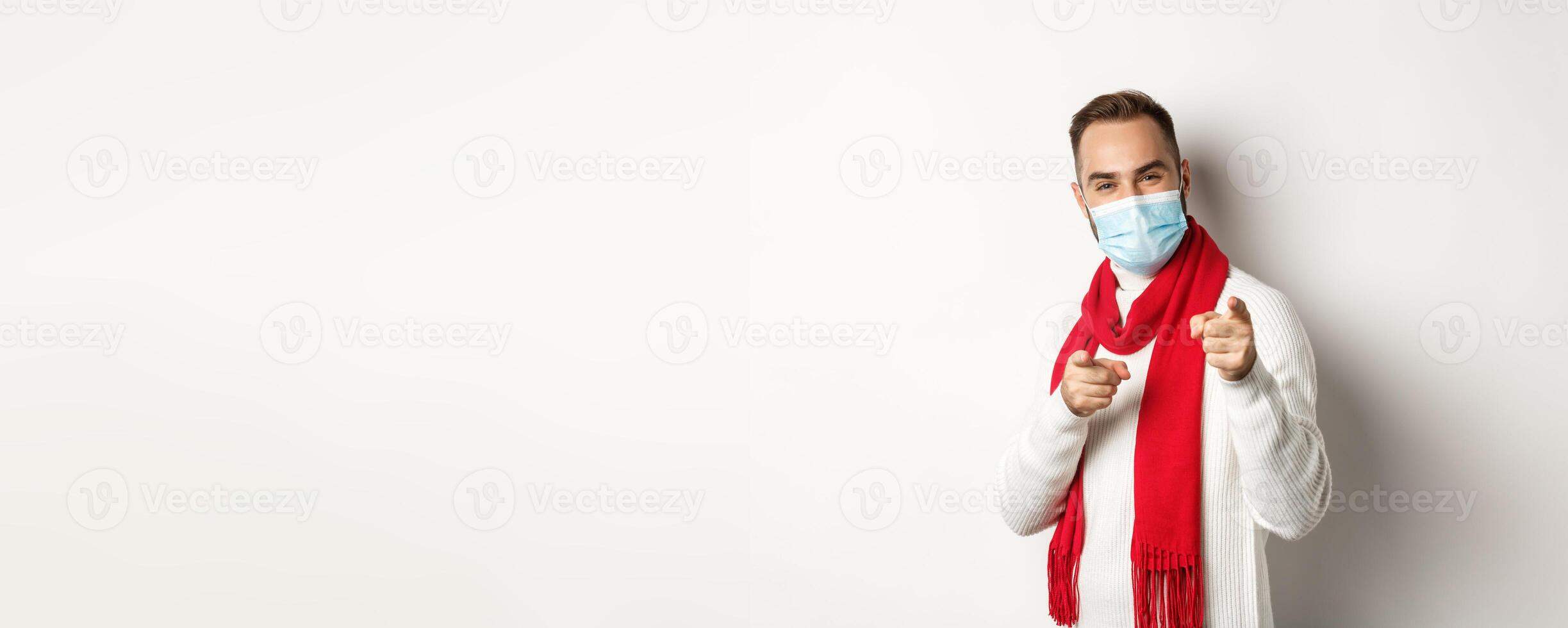 Covid-19, lockdown and quarantine concept. Happy man in face mask pointing at you, praising or saying congrats, white background photo