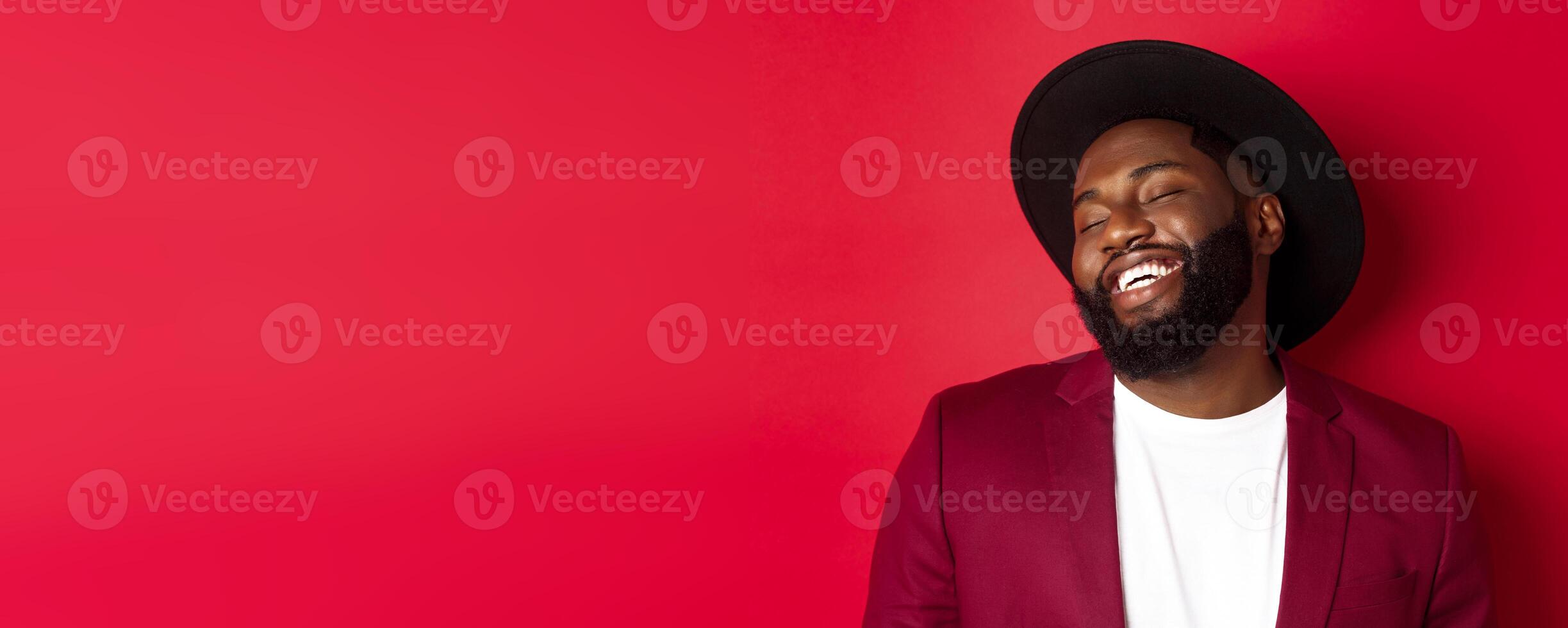 Close-up of handsome Black man with long beard laughing and having fun, looking carefree, standing over red background photo