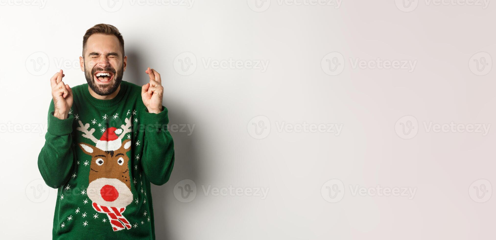 Christmas, holidays and celebration. Hopeful and excited guy making wish, keep fingers crossed for good luck and smiling, standing over white background photo