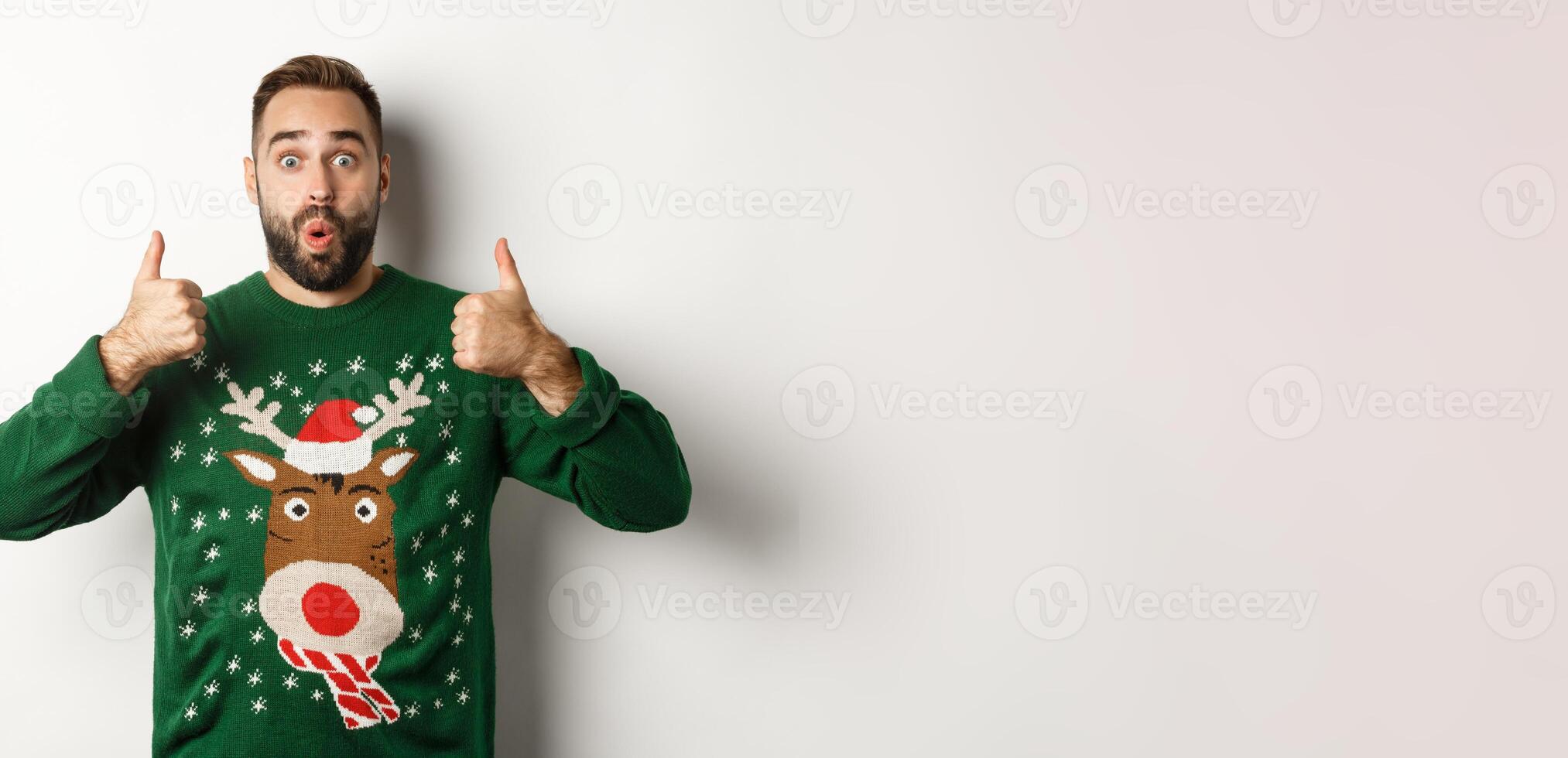 Christmas, holidays and celebration. Surprised young man in green sweater, showing thumbs up in approval, like something great, standing over white background photo