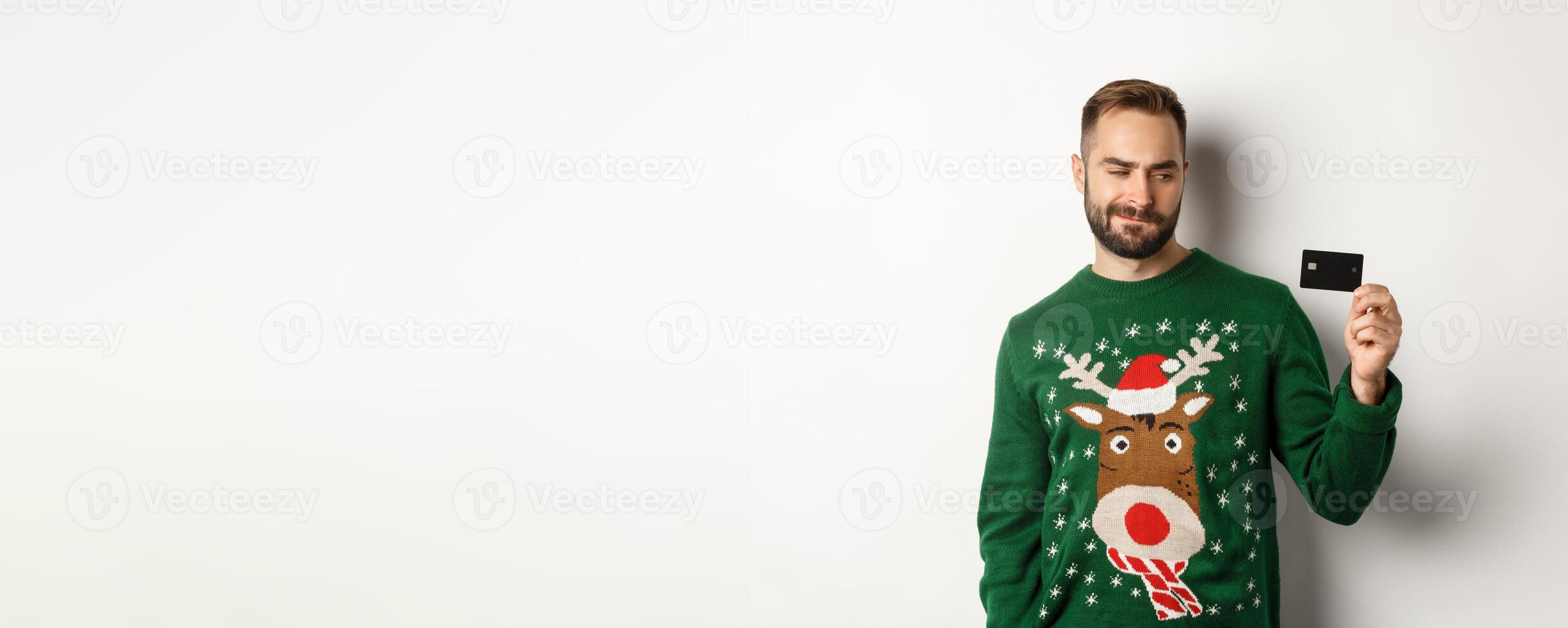 Christmas holidays and shopping concept. Thoughtful man looking at credit card, thinking and standing over white background photo