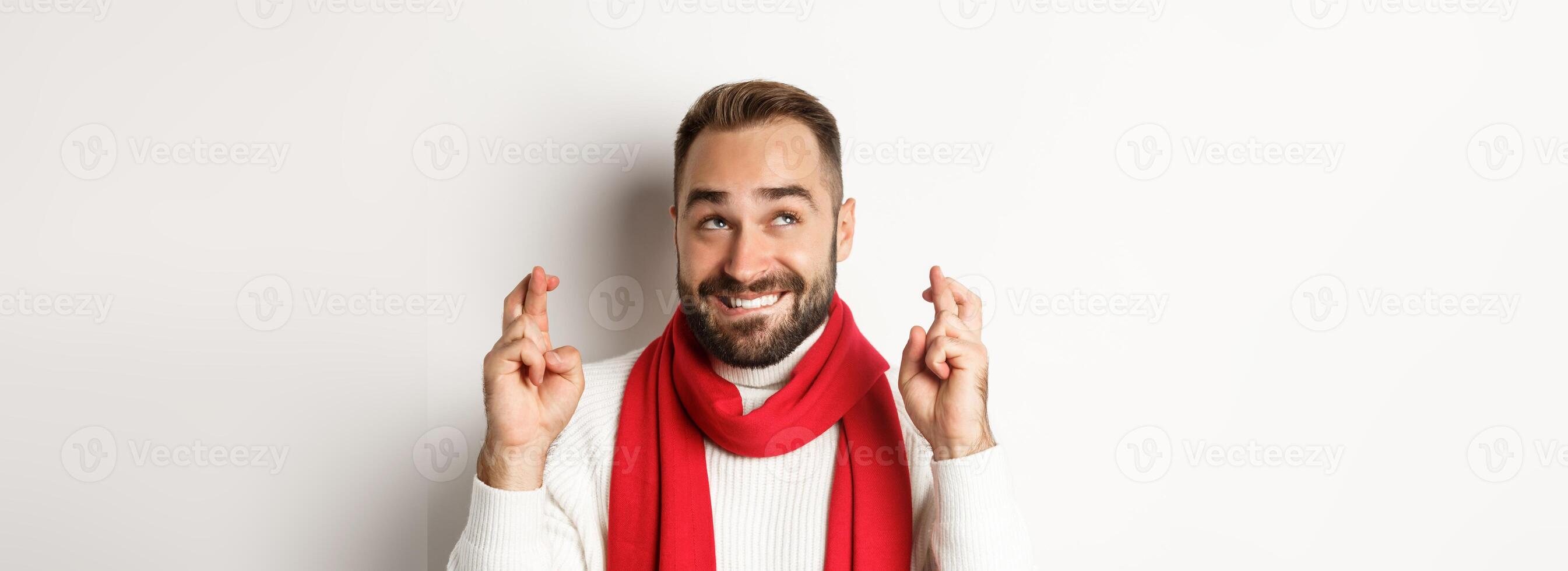 Christmas holidays. Happy attractive man making wish on winter holidays, cross fingers for good luck, looking up, standing over white background photo