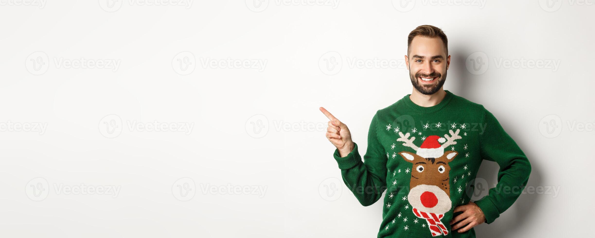 New year celebration and winter holidays concept. Confident and happy man with beard, wearing christmas sweater, pointing at upper left corner banner, white background photo