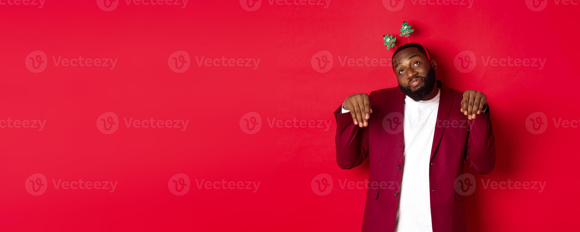 Merry Christmas. Silly and funny Black man in party headband, imitating bunny or cute puppy, standing over red background photo