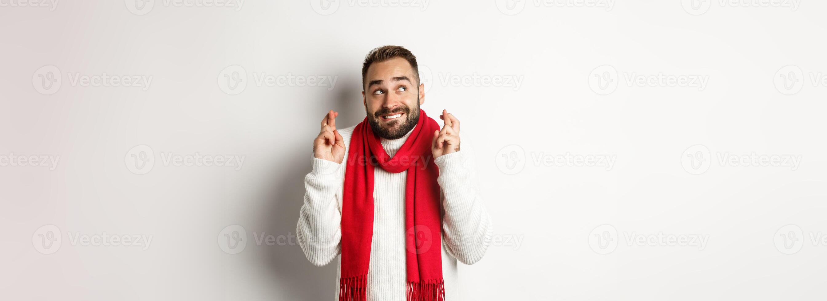 Christmas holidays and New Year concept. Hopeful man making wish with fingers crossed, waiting for gifts, standing over white background photo