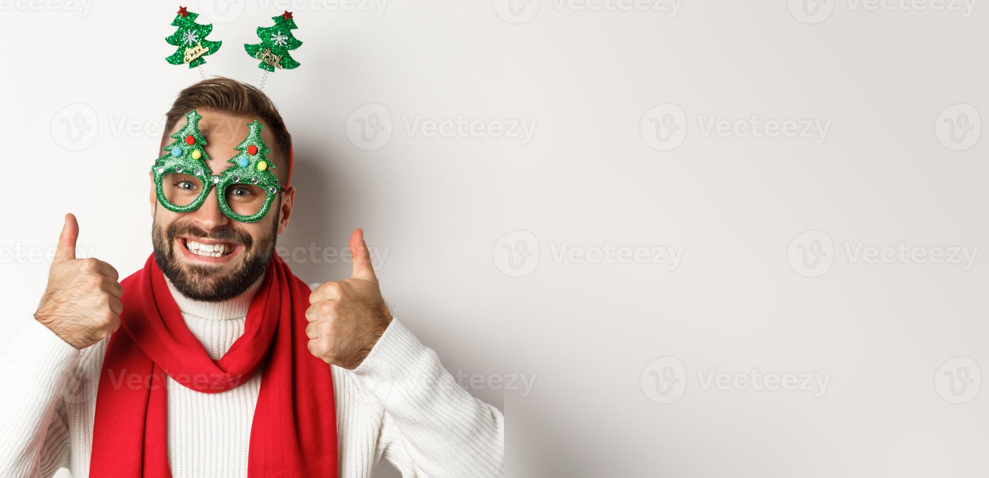 Christmas, New Year and celebration concept. Close-up of handsome bearded man in funny party glasses looking happy, showing thumb up in approval, like something, white background photo