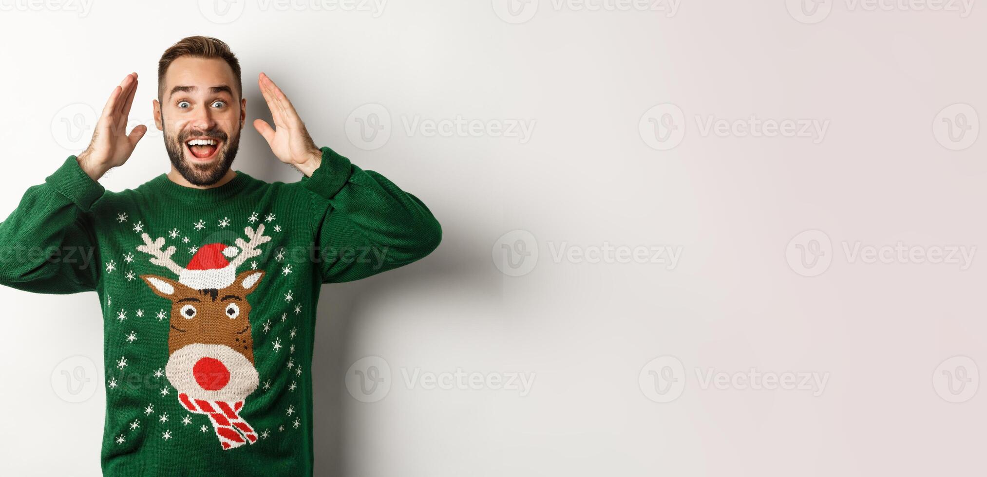 Christmas, holidays and celebration. Surprised man open eyes and see a gift, standing happy against white background photo