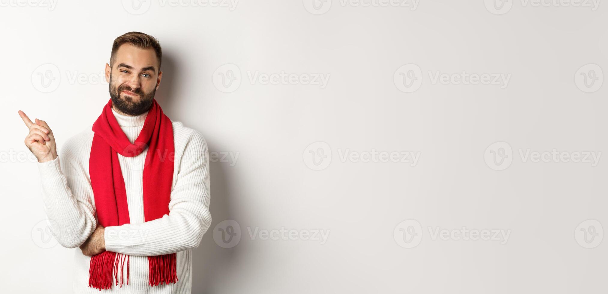 Christmas shopping and winter holidays concept. Skeptical young man showing something bad, pointing finger left and grimacing displeased, standing over white background photo