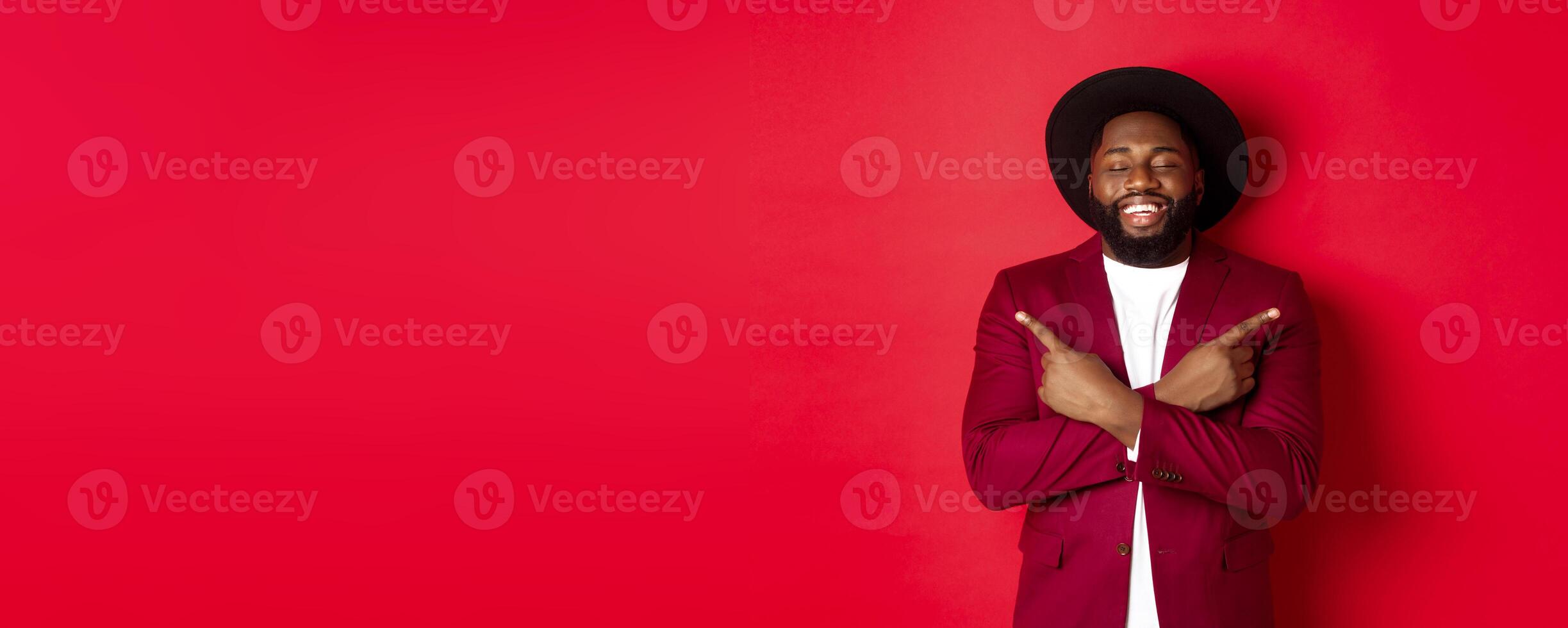 Happy young man dreaming and pointing fingers sideways, close eyes and smiling, showing two things, standing over red background photo