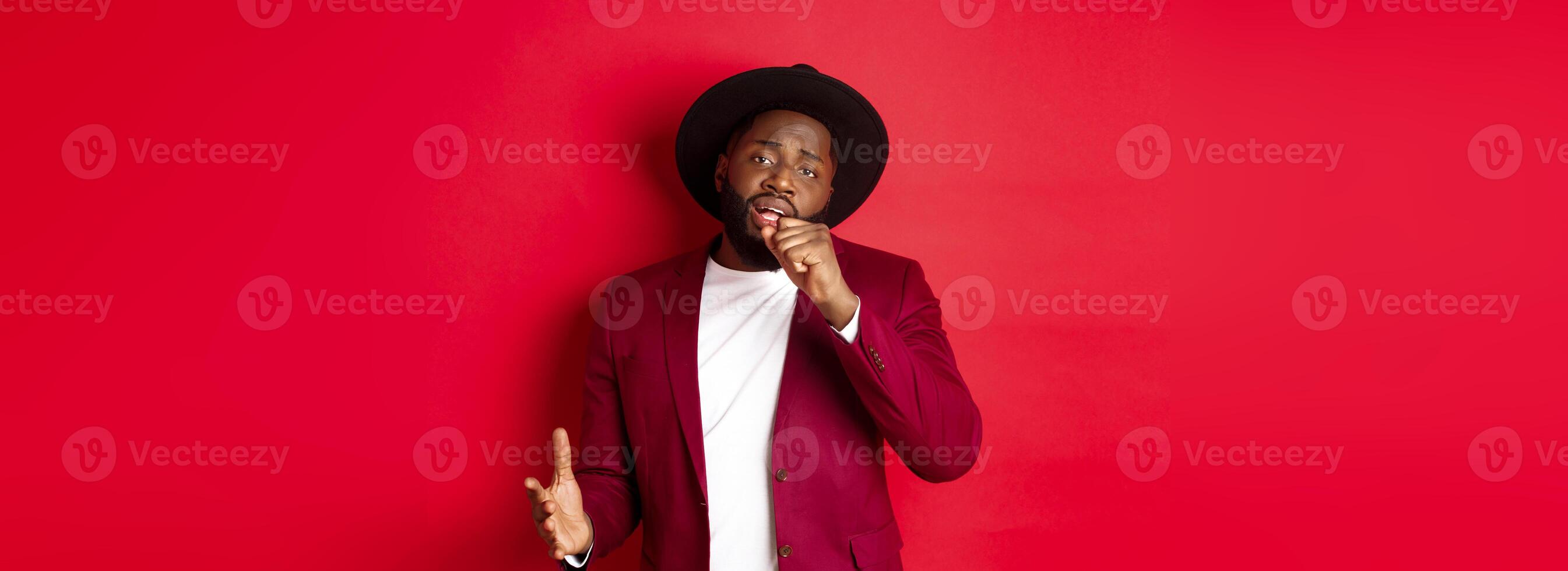 Christmas shopping and people concept. Handsome Black male model in party outfit singing in invisible microphone, looking passionate at camera, red background photo