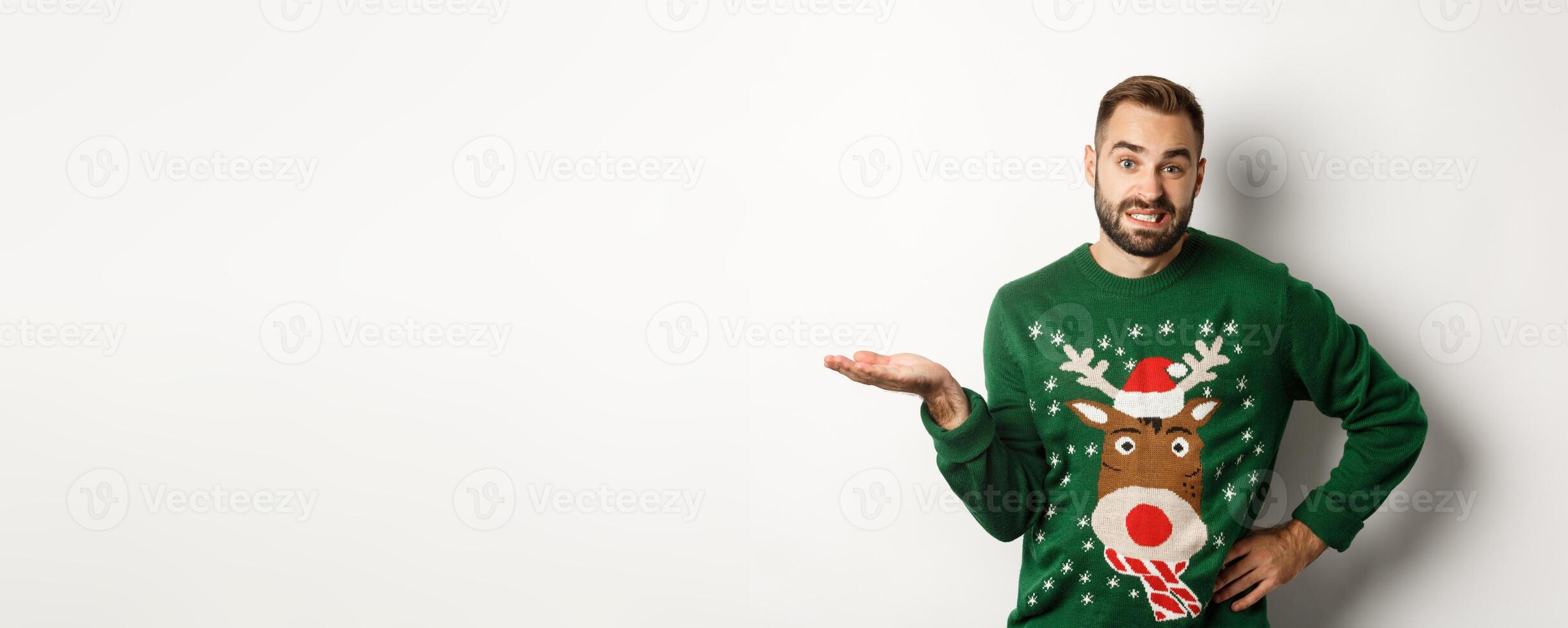 New Year, holidays and celebration. Confused bearded guy in funny sweater, shrugging and looking clueless, dont know, looking awkward, standing over white background photo