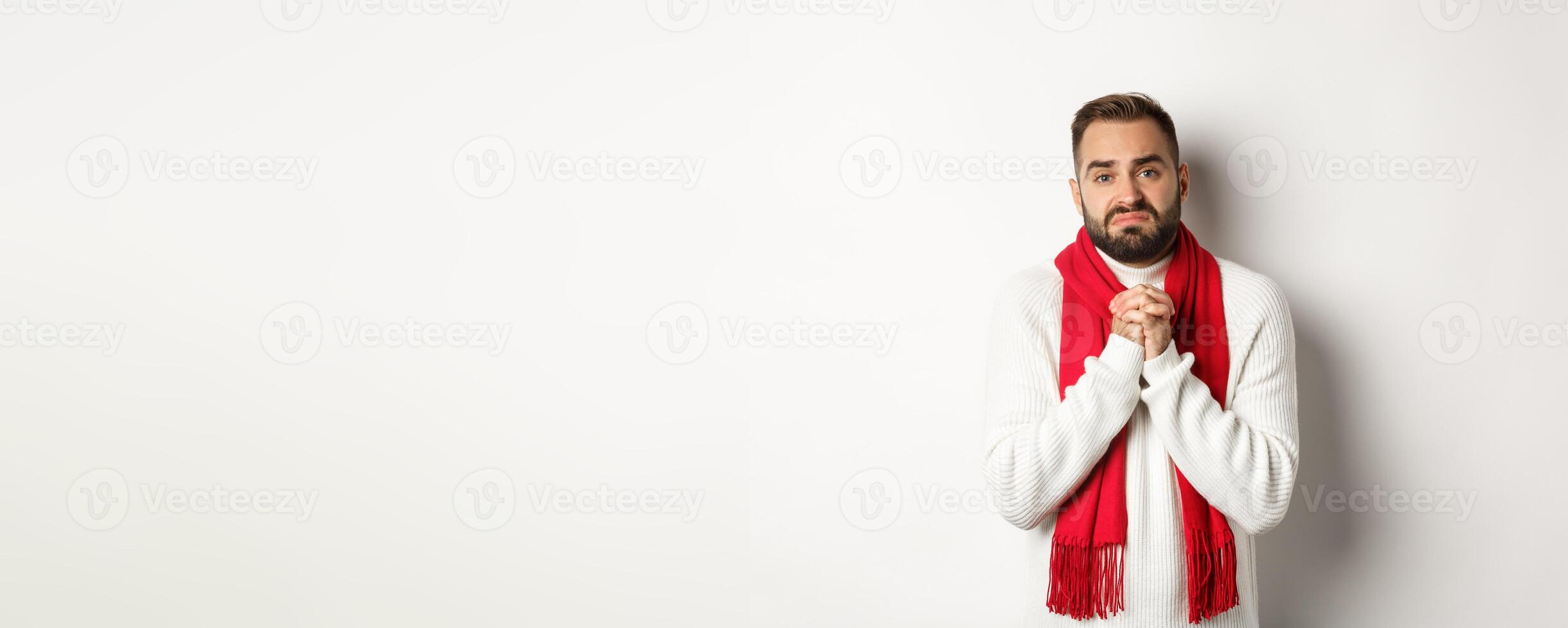 Christmas holidays and New Year concept. Sad man begging for help, holding hands in pray and looking distressed at camera, asking for favour, standing over white background photo