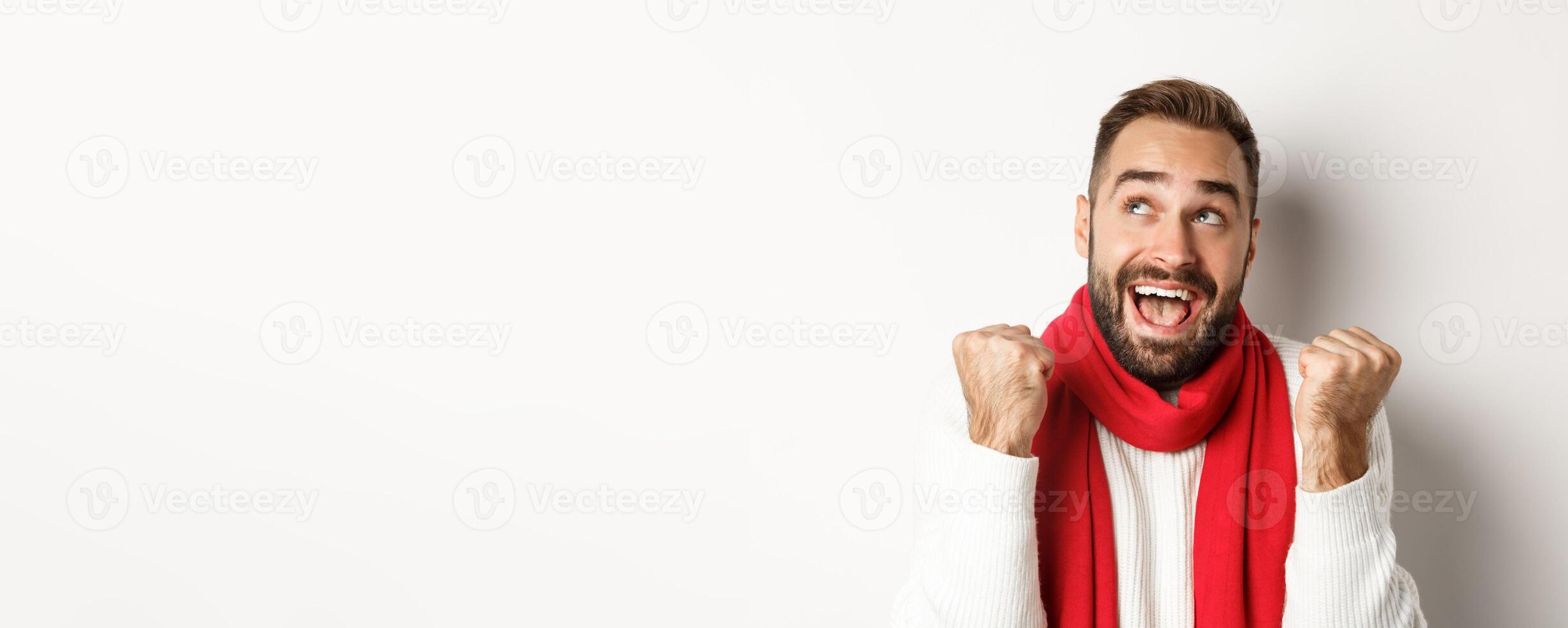 Christmas holidays. Close up of handsome man feeling excited about New Year party, fist pump and looking up amazed, white background photo
