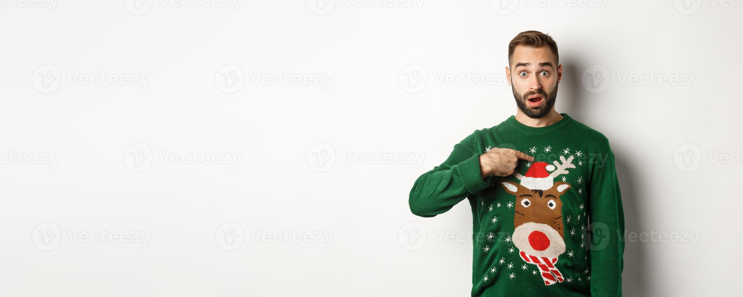 Winter holidays and christmas. Confused bearded guy pointing at himself, being startled with offer, standing over white background in sweater photo