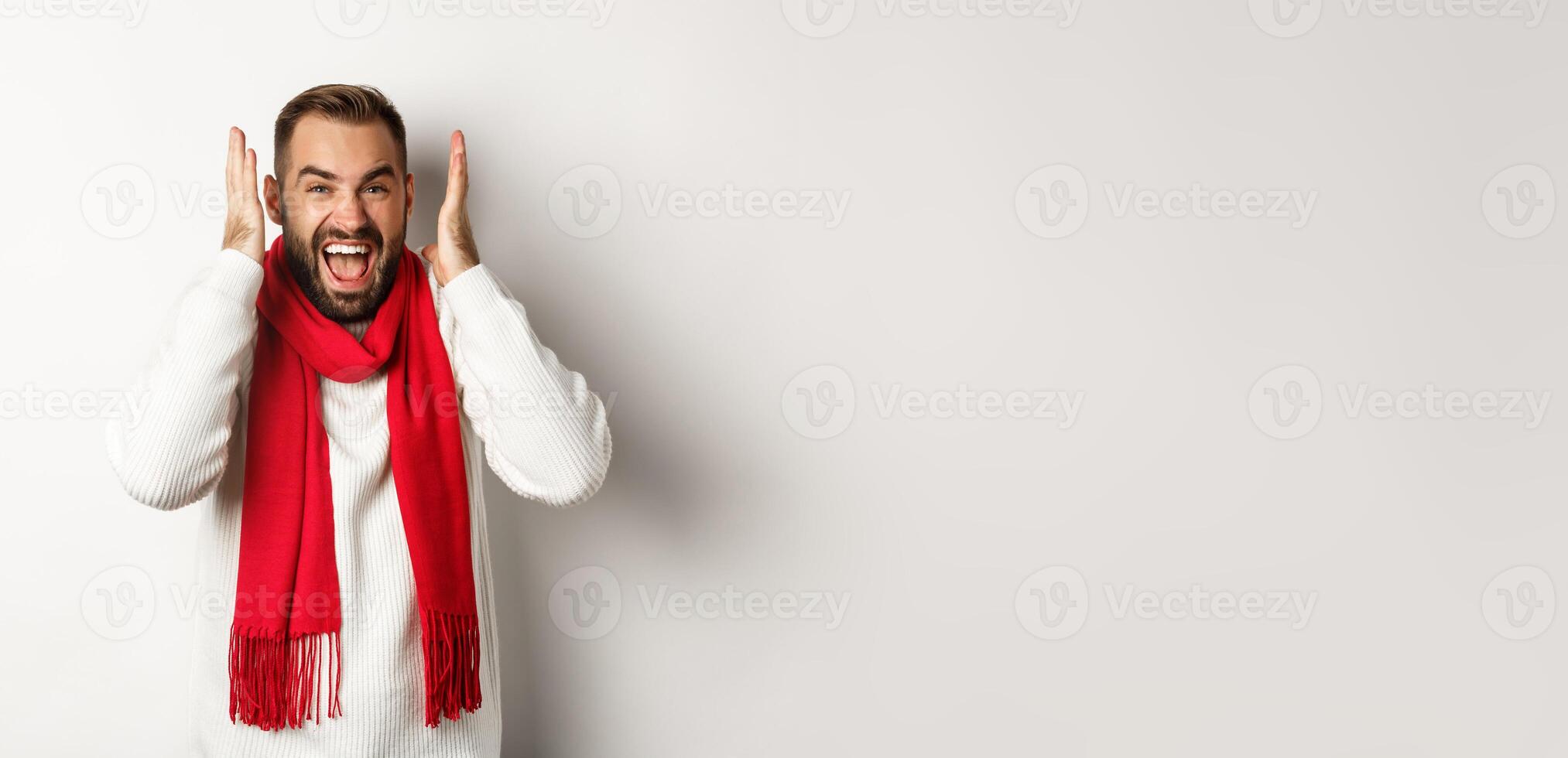 Christmas holidays and New Year concept. Angry man in scream and shout, shaking hands near head with frustrated expression, standing over white background photo