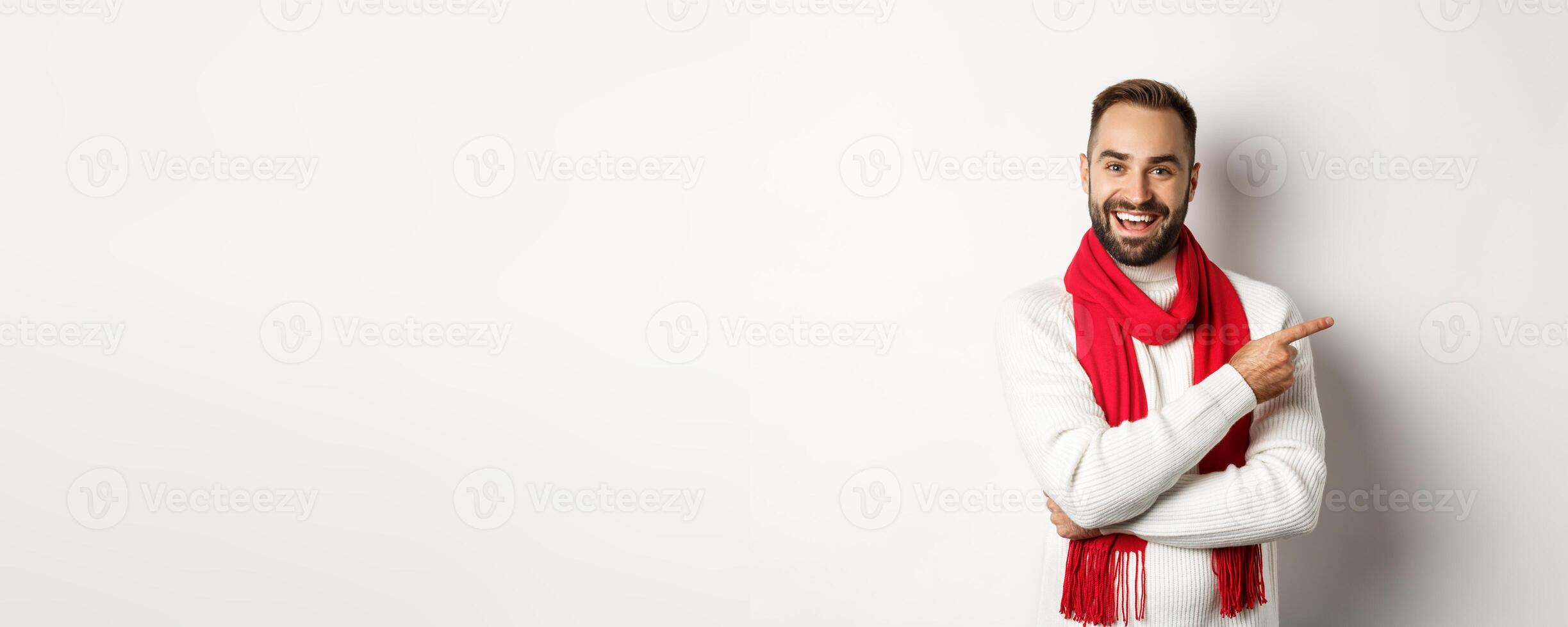 Christmas holidays and celebration concept. Happy bearded man pointing finger right at copy space, showing advertisement offer, standing over white background photo