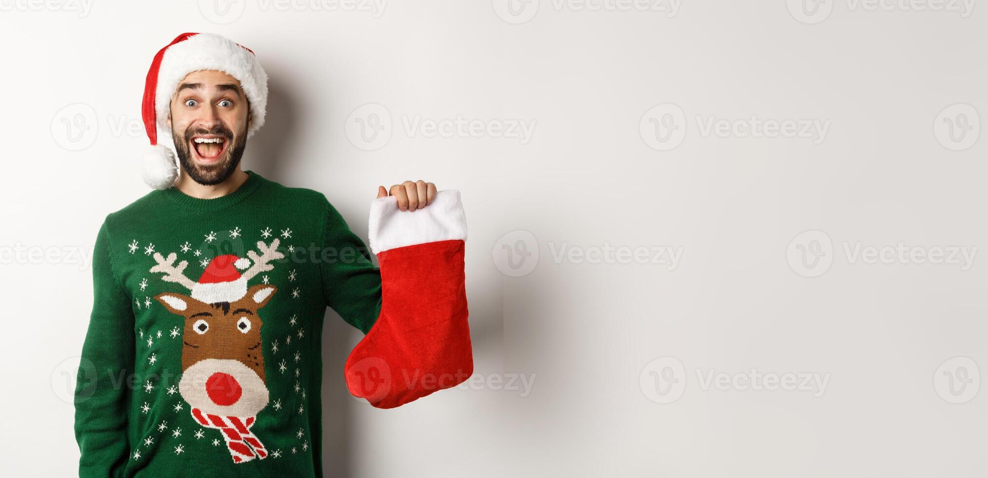 Xmas and winter holidays concept. Happy man got a gift in Christmas sock, looking excited, standing in Santa hat against white background photo