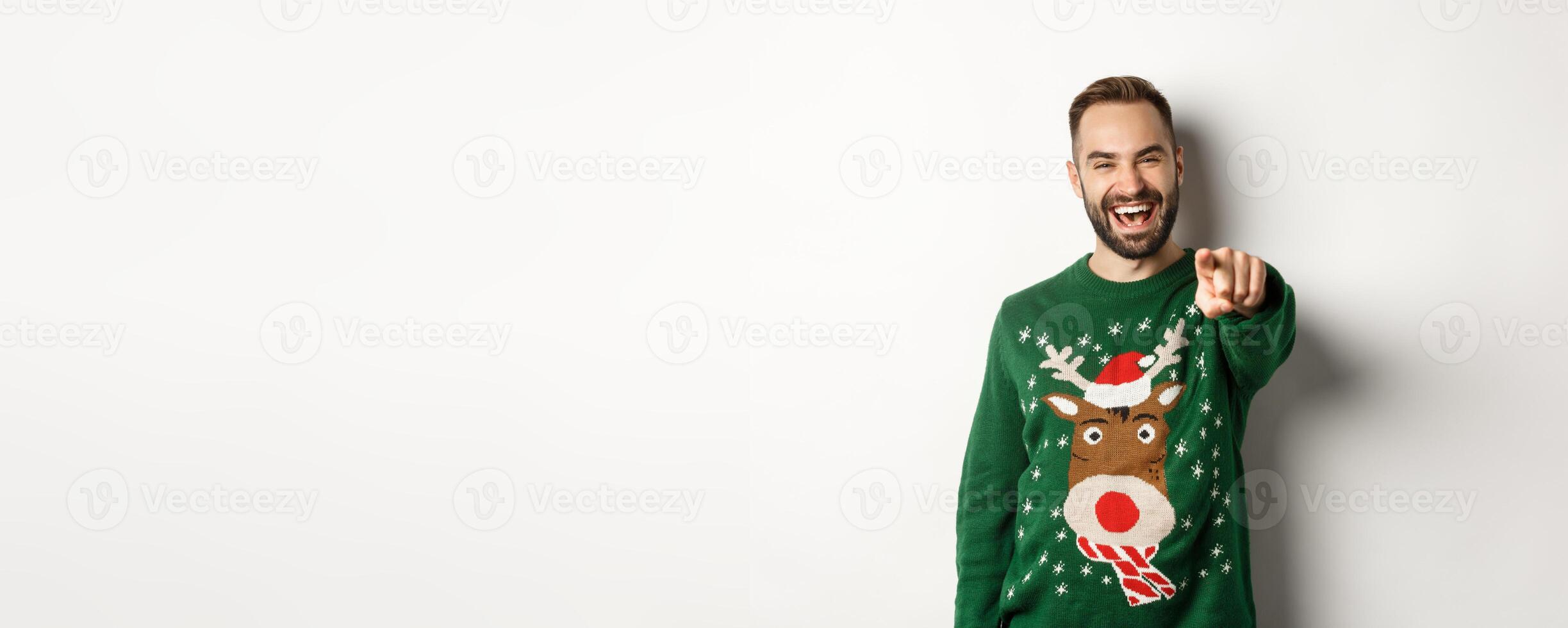 Winter holidays and christmas. Happy young man celebrating New Year eve, pointing finger at you and laughing, standing over white background photo