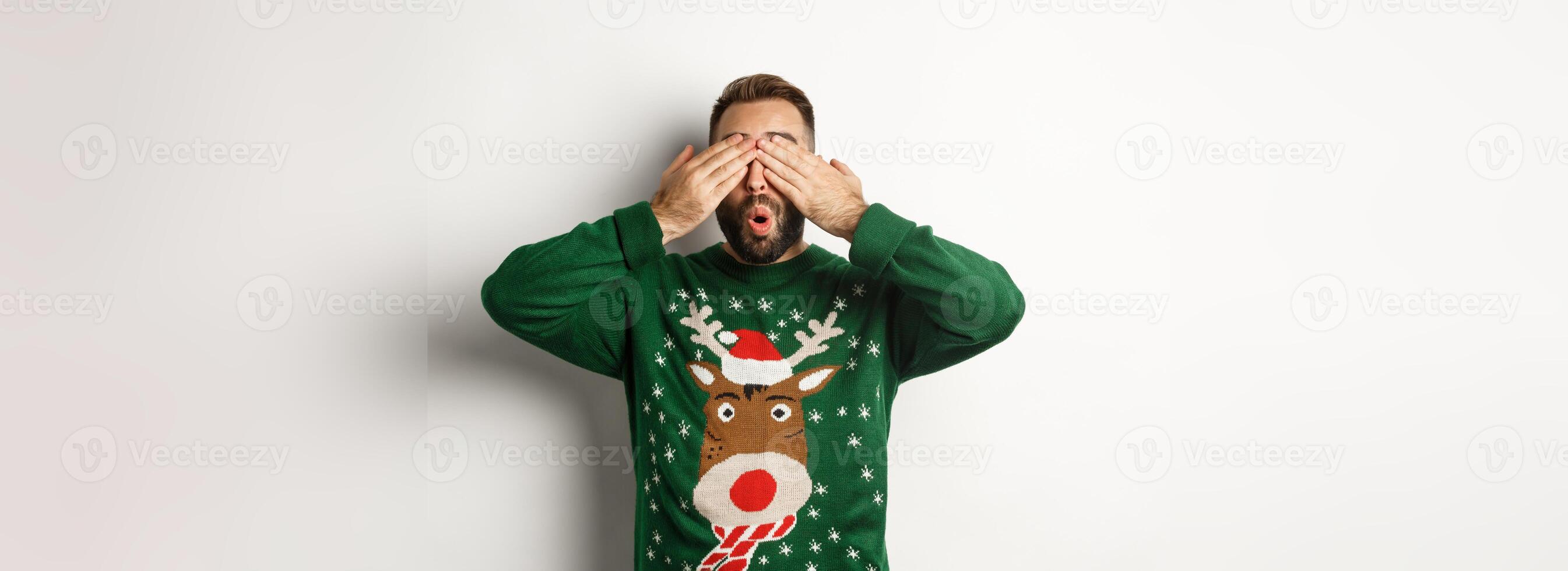 Christmas, holidays and celebration. Happy young man shut eyes and smiling, waiting for surprise gift, standing over white background photo