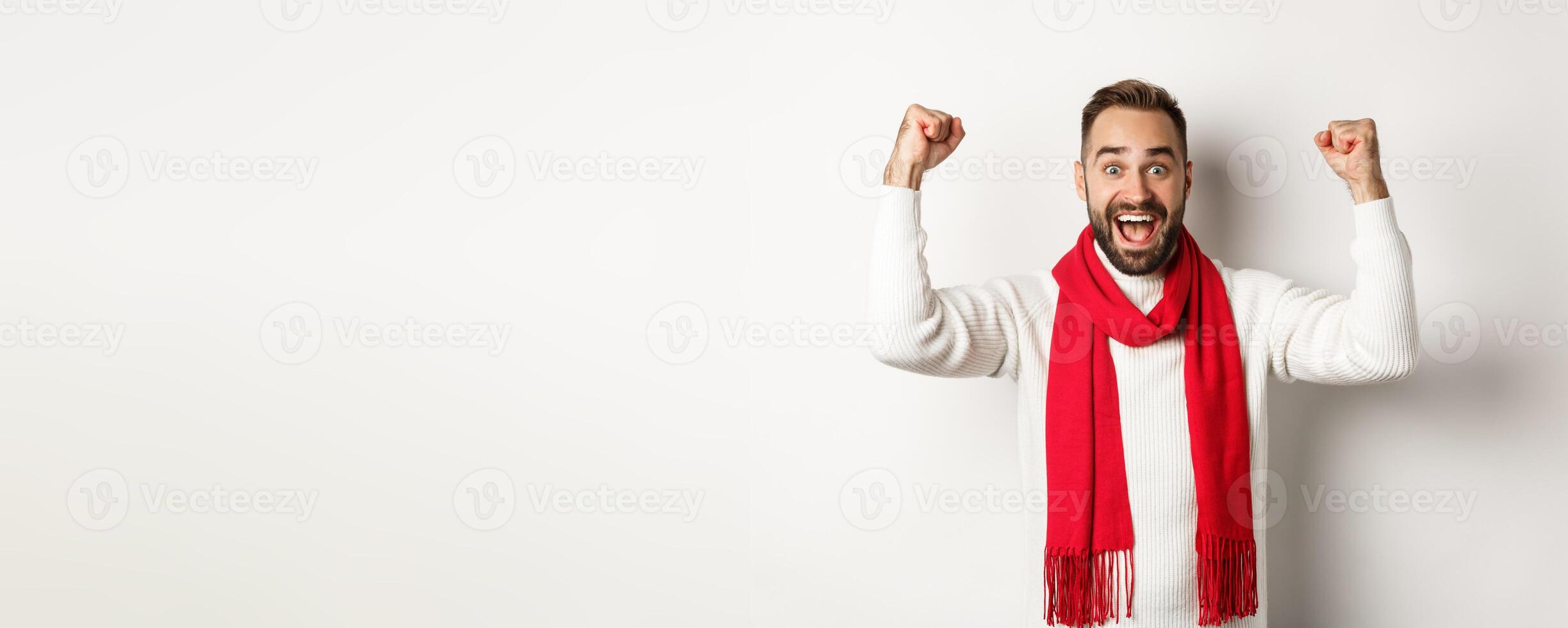 Christmas holidays and New Year concept. Excited man rejoicing, winning prize, raising hands up and looking relieved, triumphing, standing over white background photo