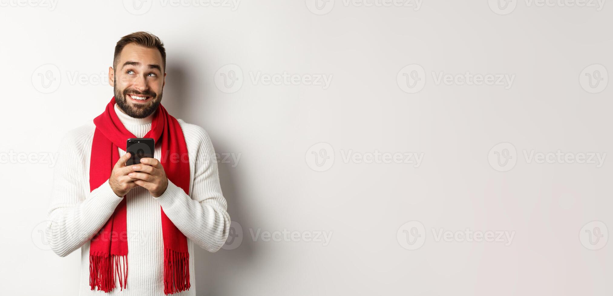 Man thinking while texting message on mobile phone, smiling and standing over white background photo
