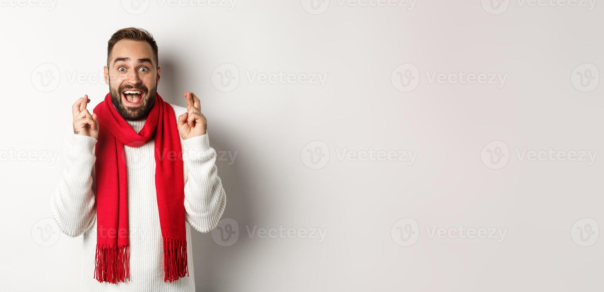 Christmas holidays and New Year concept. Hopeful man making wish with fingers crossed, waiting for gifts with excitement, standing over white background photo
