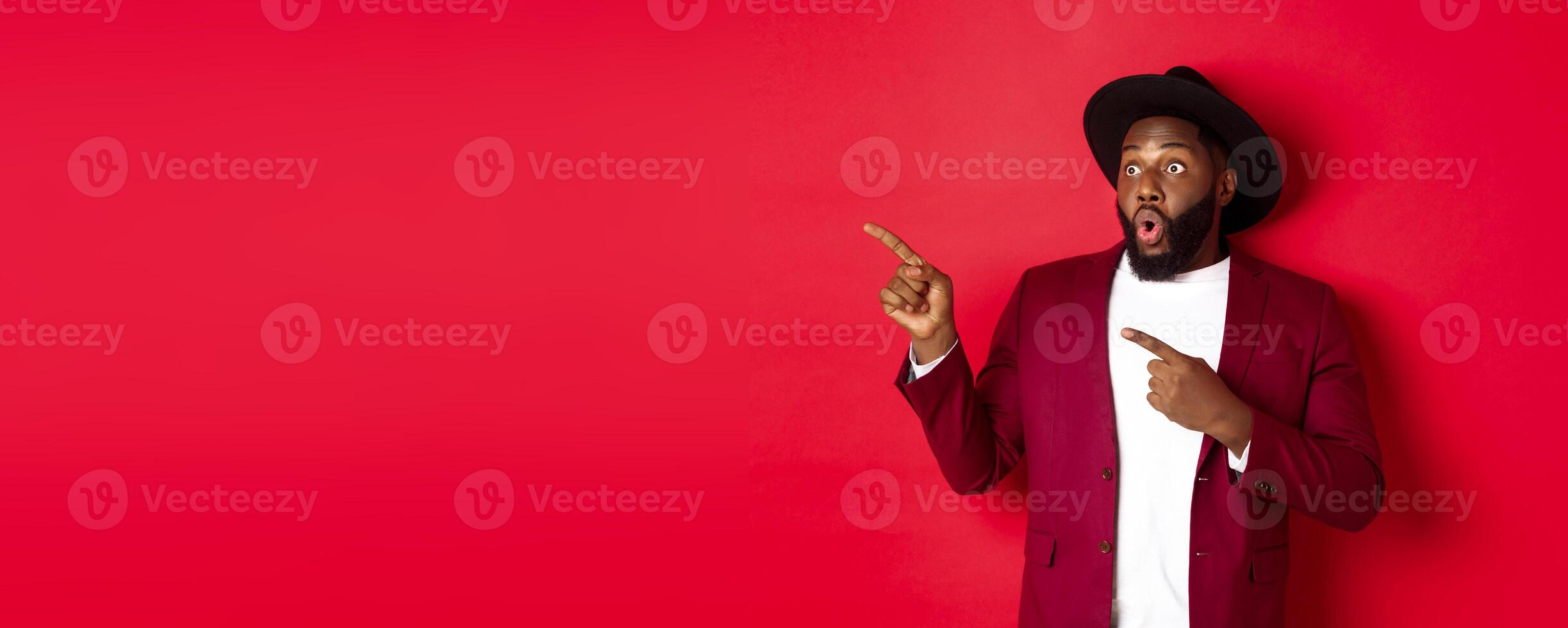 Winter holidays and shopping concept. Happy Black man pointing left and smiling, showing new year promo offer on red background photo