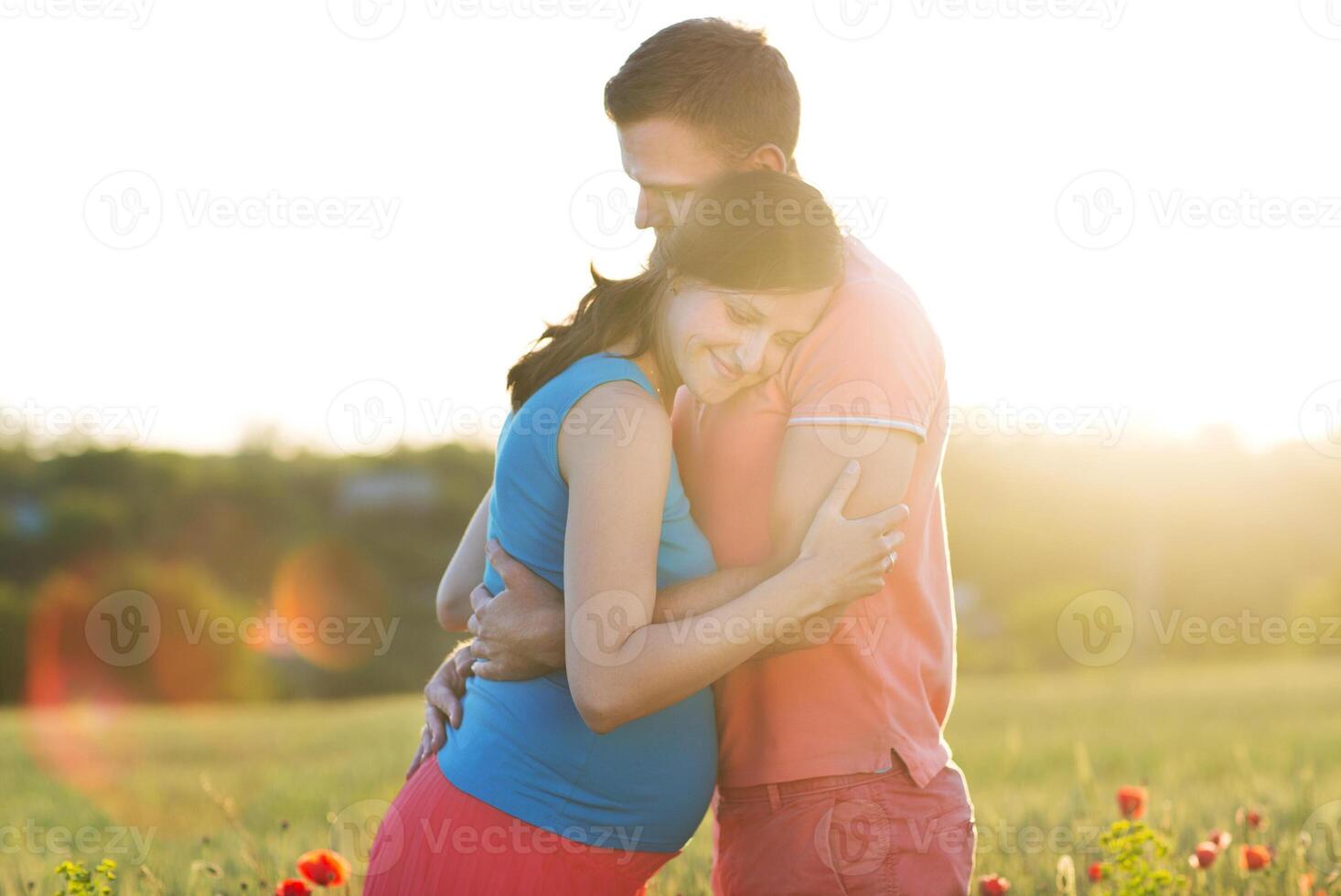 Young beautiful pregnant couple in poppy field photo
