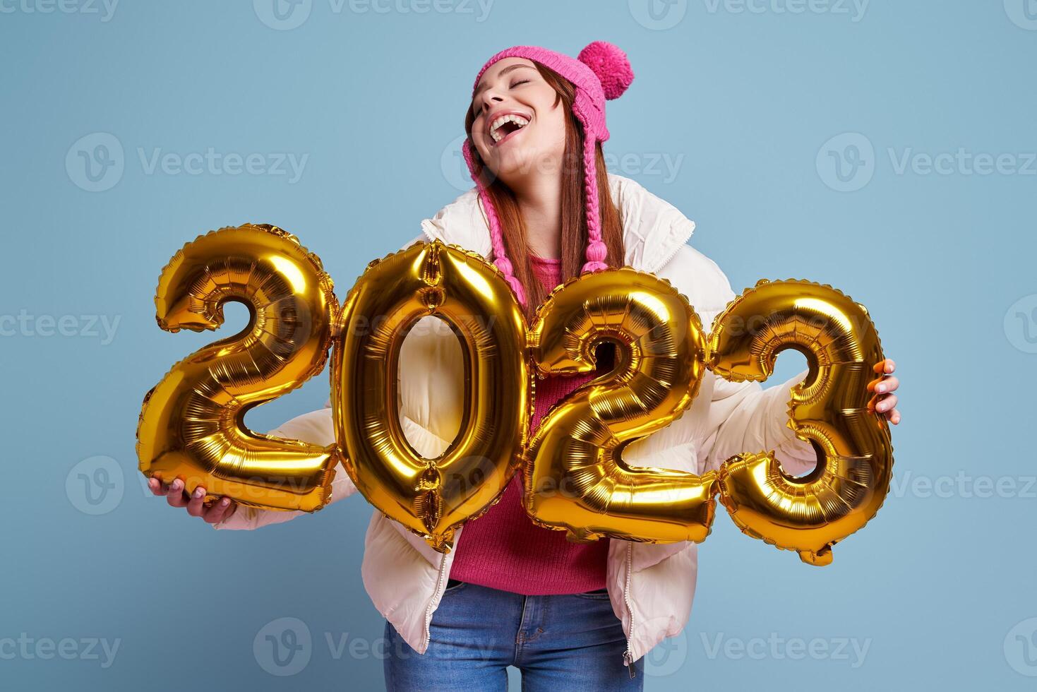 Happy young woman in winter coat holding gold colored numbers against blue background photo