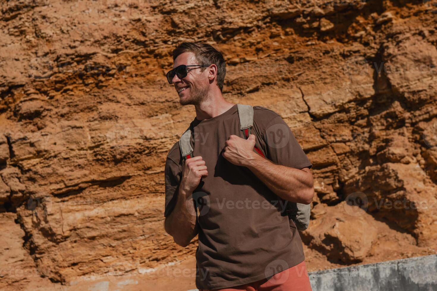 Happy male adventurer with backpack standing against the rocky mountain outdoors photo