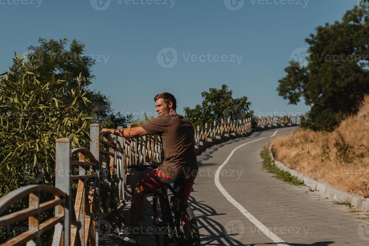 Handsome young man on bicycle resting after riding bicycle by the scenic road photo