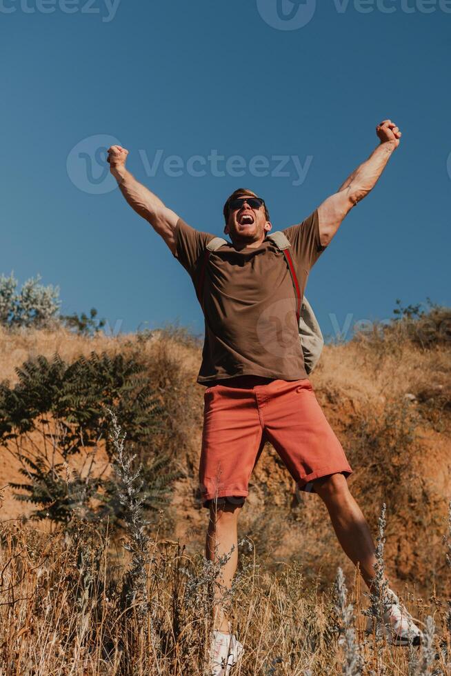 Joyful male adventurer with backpack gesturing while hiking in mountains photo