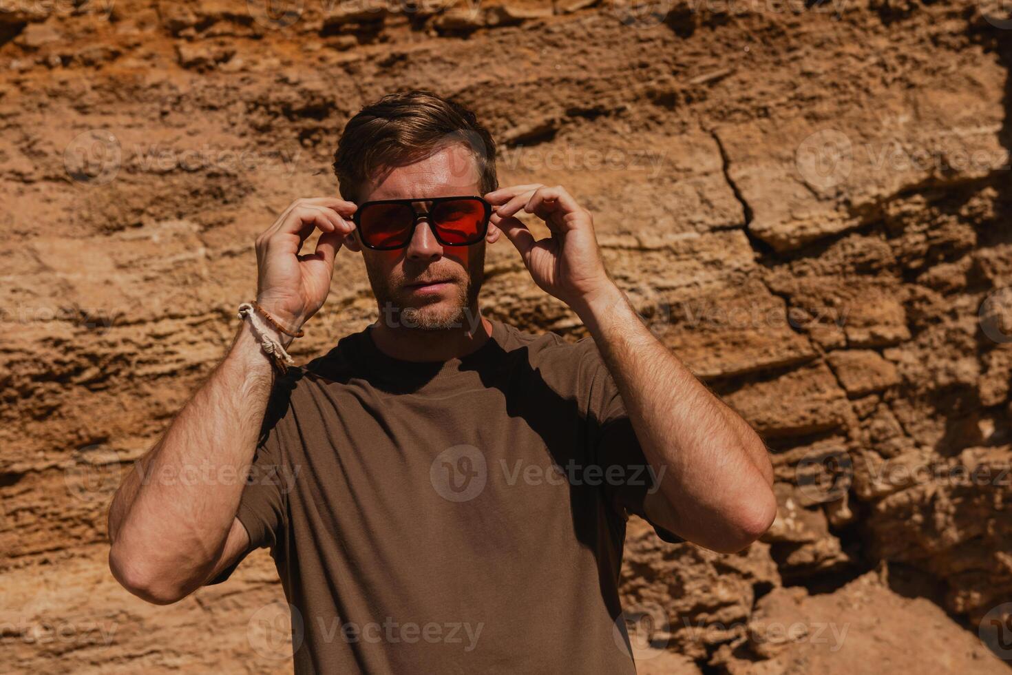Handsome young man adjusting his trendy glasses while standing against a rocky mountain photo