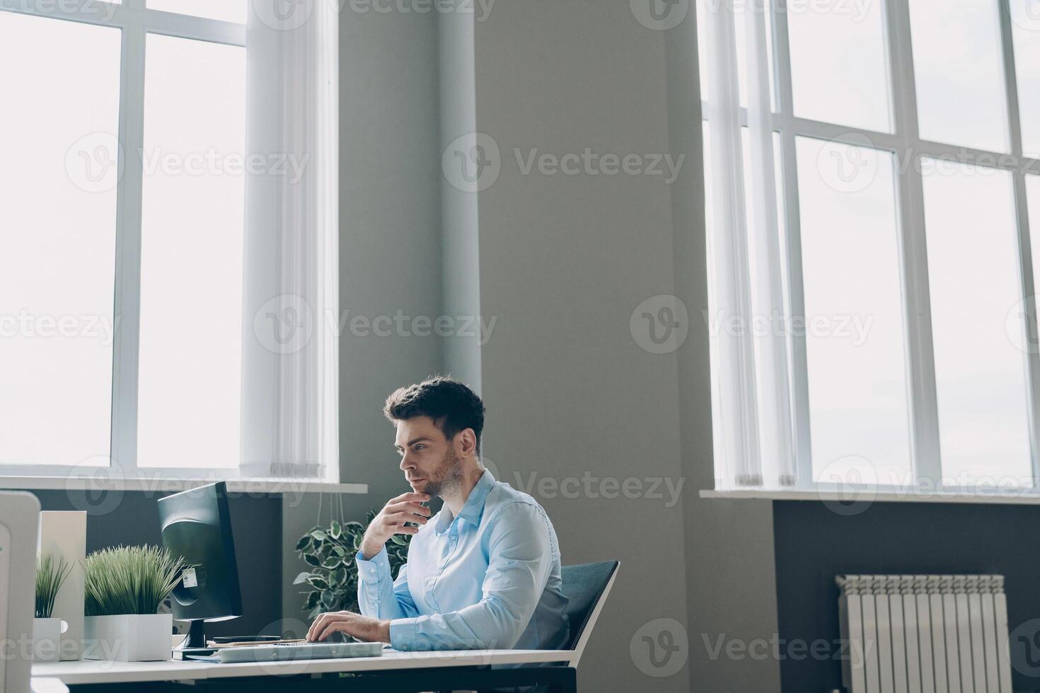 Confident young businessman using computer while sitting at his working place in office photo