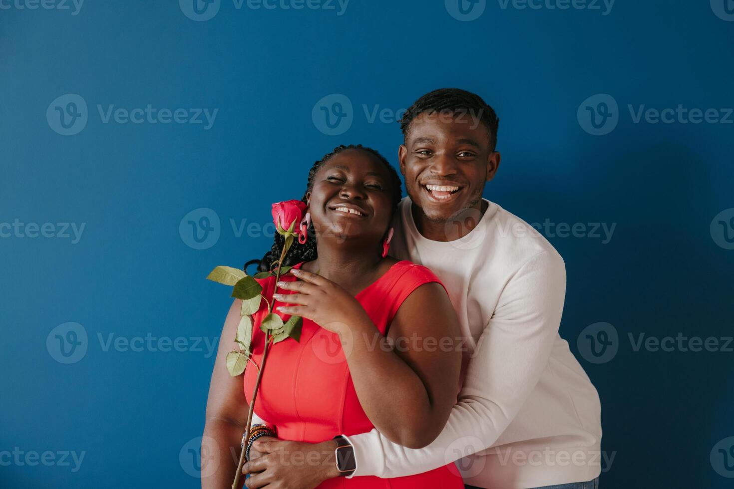 Happy young African man embracing his girlfriend holding red rose on blue background photo