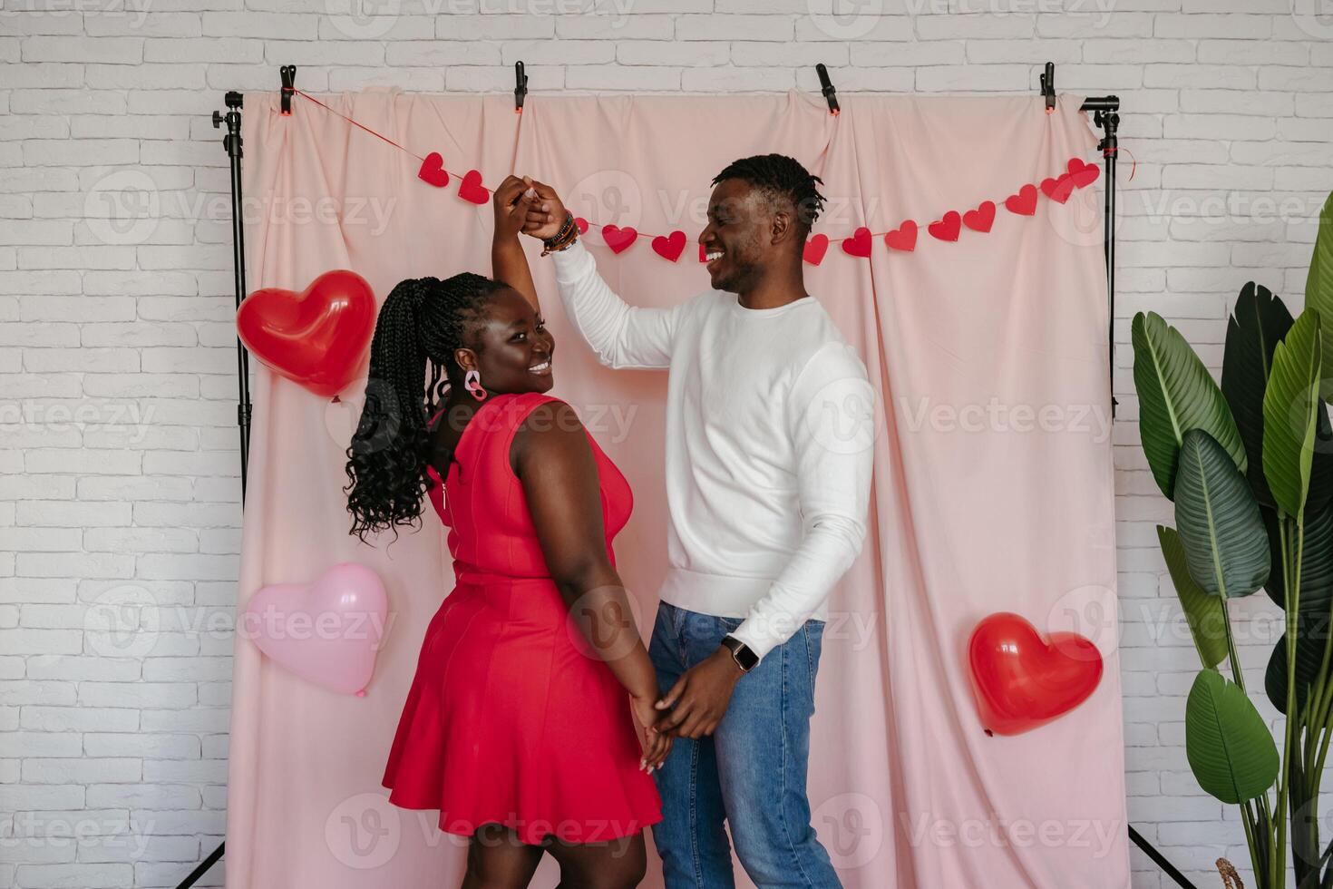 Romantic young African couple dancing on pink fabric background with heart shaped balloons photo