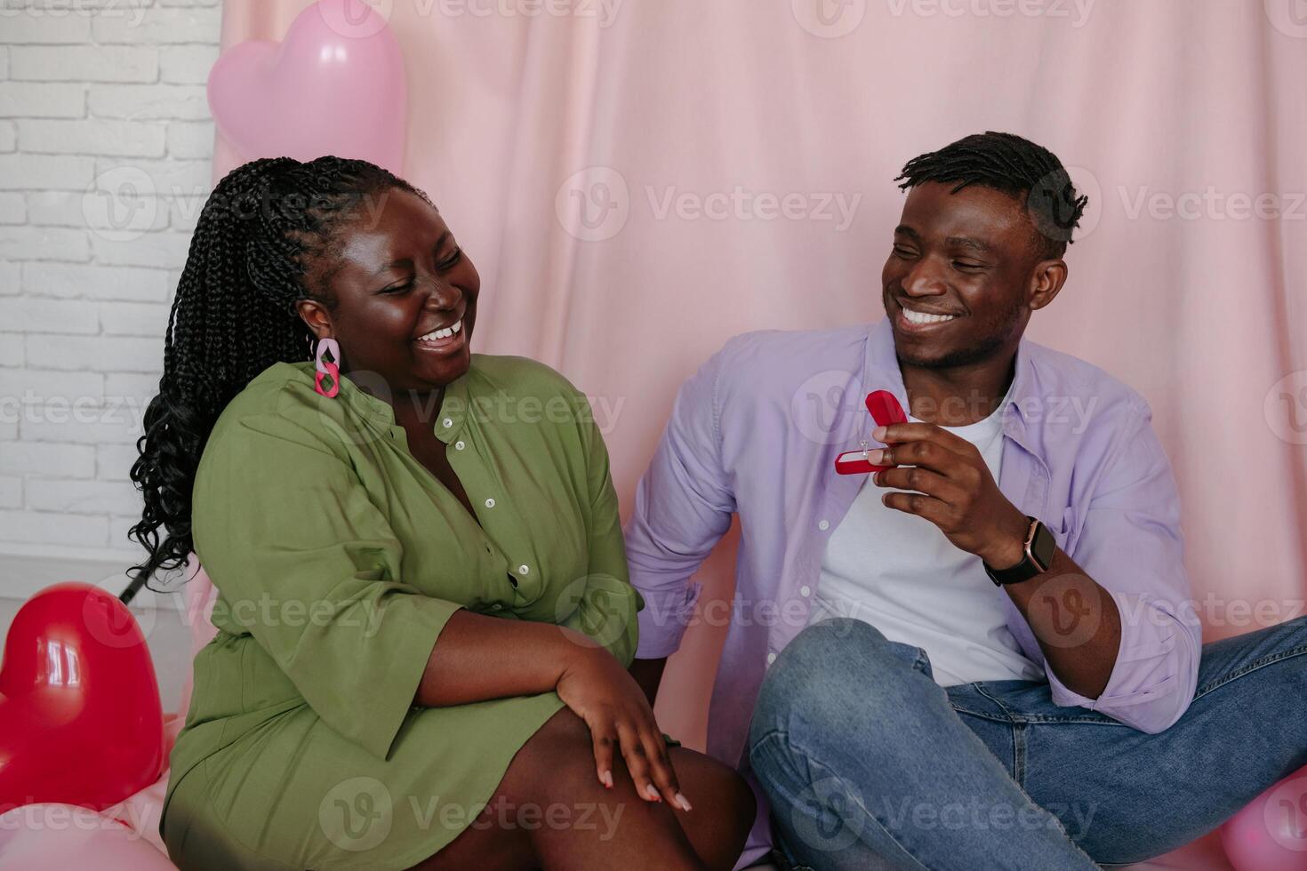 Handsome African man giving engagement ring while proposing his girlfriend to marry him on pink background photo