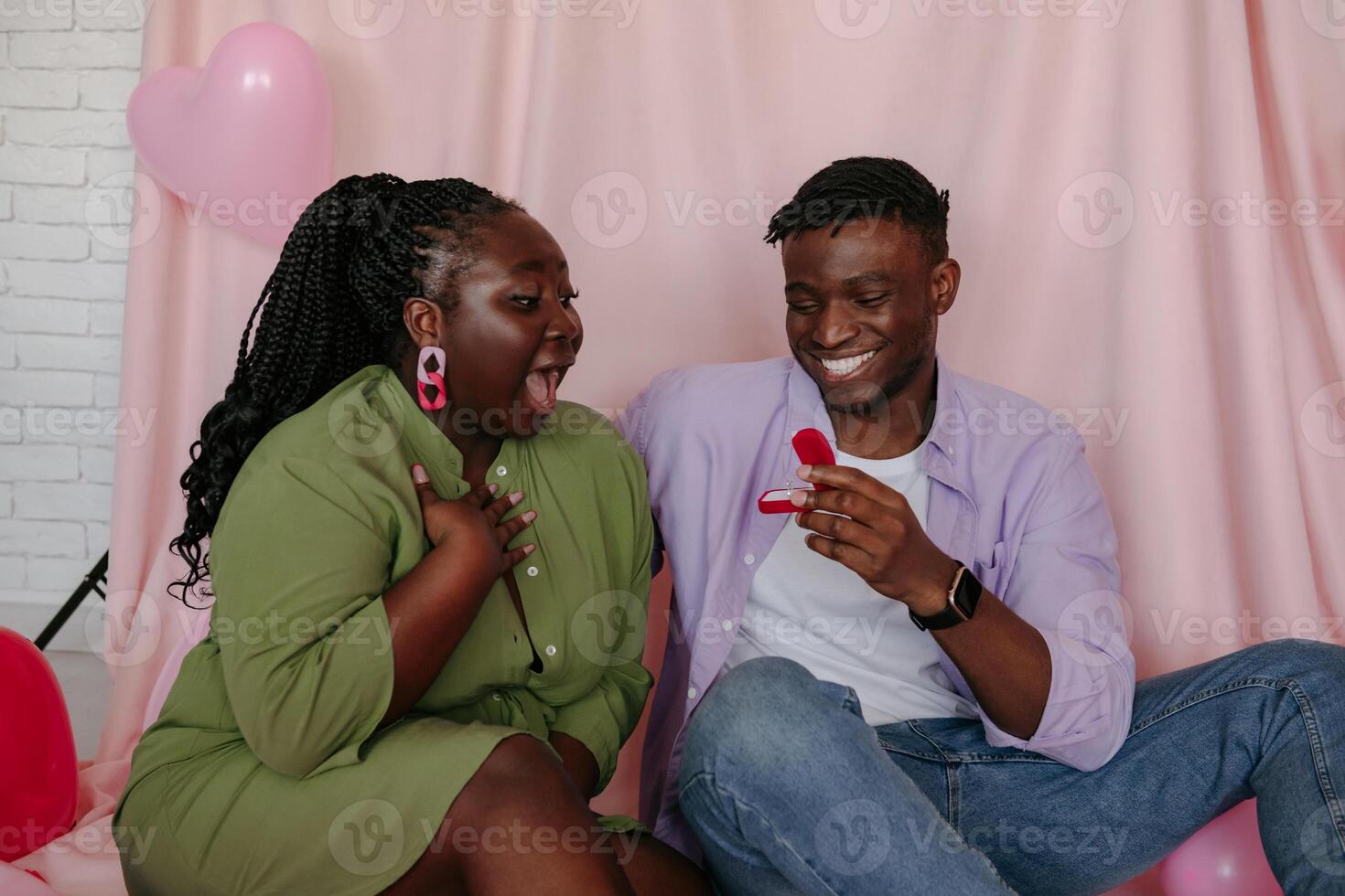 Handsome African man giving engagement ring while making proposal to his girlfriend on pink background photo