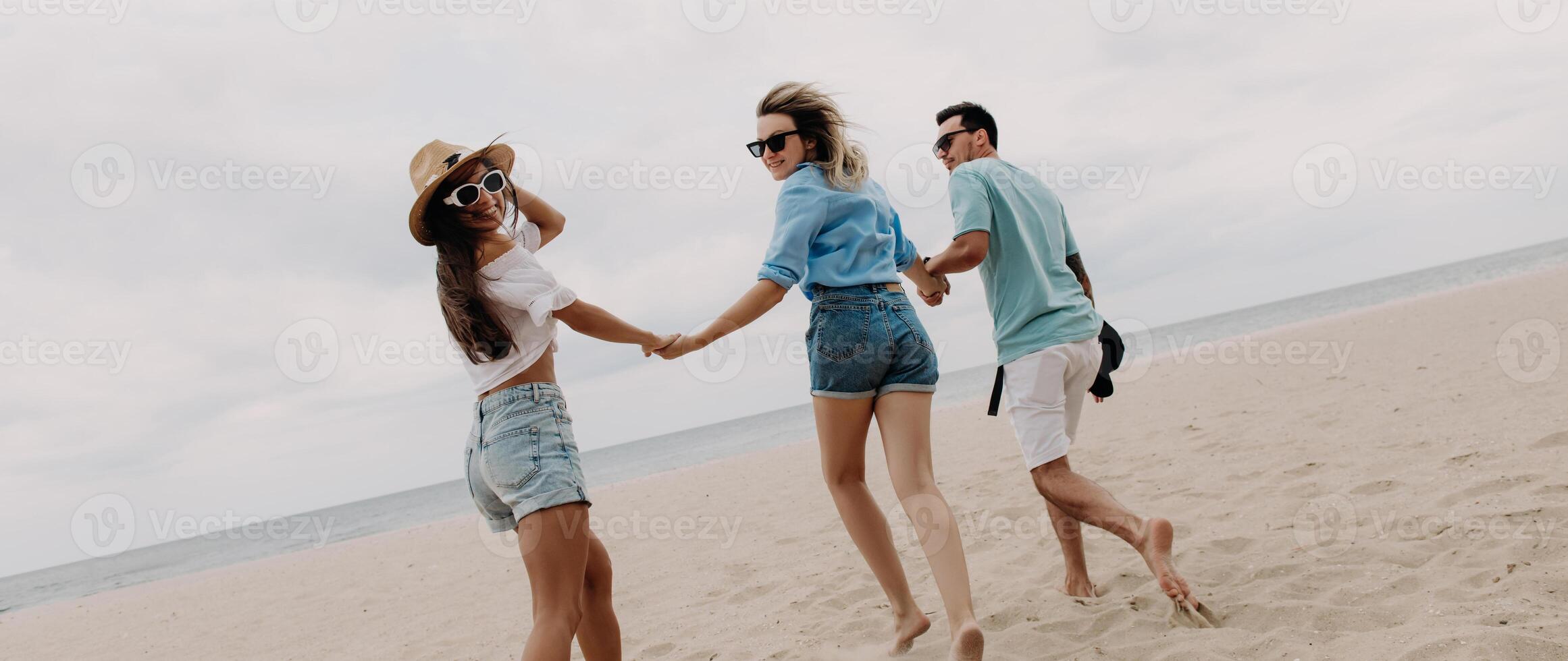 Three joyful friends spending fun time while running by the beach to the sea together photo